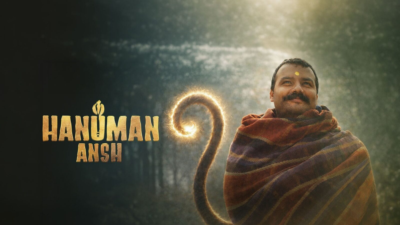 Banner for the film Hanuman Ansh: a man wrapped in a striped shawl looks upward in a misty forest, with a glowing tail curling beside him and the film's gold title logo at left.